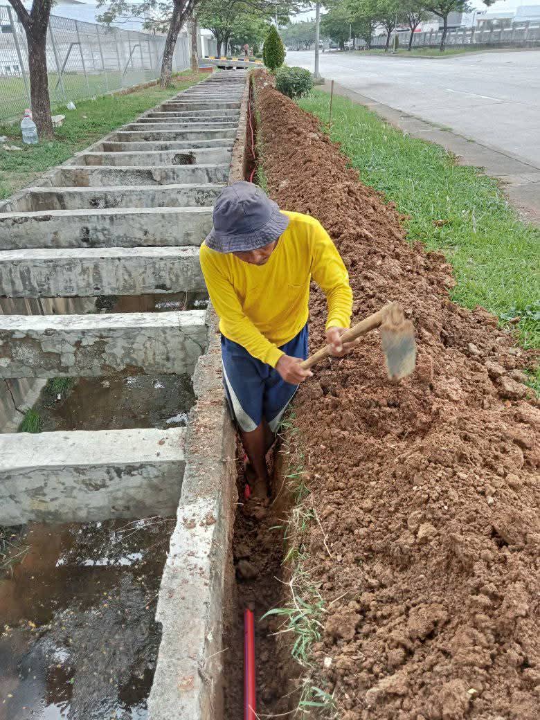 Pekerja melakukan instalasi pipa di dalam galian open-cut yang rapi